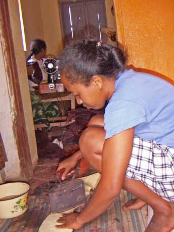 12. Ironing. Mme Bako irons the woven raffia before sewing. Re-hot coal is put into the iron.